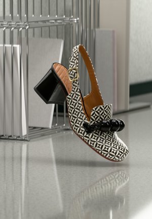 Chaussure à talons avec bride arrière en motif géométrique noir et blanc, finition lisse semblable au cuir et décoration en perles rondes à l'avant.