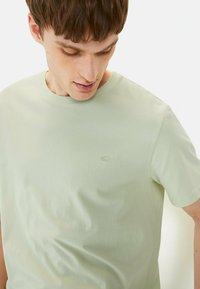 Lys grøn kortærmet t-shirt lavet af blød bomuld med rund hals og diskret broderet logo på brystet. Glat tekstur.