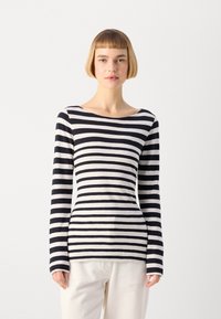 Långärmad topp med marinblå och vita horisontella ränder, rund halsringning, tillverkad av ett mjukt material, figursydd design, bärs tillsammans med krämfärgade byxor.