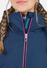 Marinejacke mit pinkem Reißverschlussakzent und Logodetails; Reißverschlusskragen; weiche Textur; geflochtenes Haar sichtbar.