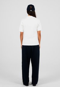 Biała koszula z krótkim rękawem zestawiona z luźnymi ciemnonawowymi spodniami. Czapka z logo w kontrastowym kolorze. Gładka faktura materiału.