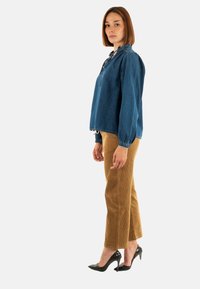 Blusa in denim blu con una vestibilità ampia, scollo arricciato e lunghe maniche a sbuffo, abbinata a pantaloni dritti in velluto a coste marroni. Tacchi alti neri.