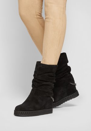 Bottes bottines en daim noir au design décontracté, avec une semelle texturée et un détail tressé. Les talons sont couverts, ce qui améliore la stabilité.
