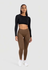Zwarte crop top met lange mouwen, gecombineerd met bruine, hoog getailleerde leggings en witte sneakers; gladde textuur, nauwsluitend ontwerp.