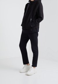 Svart hoodie med dragkedja framtill, sidofickor och texturerat tyg. Matchad med tajta svarta byxor och vita sneakers.