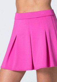 Falda plisada de un brillante color rosa, llevada en la cintura, mostrando el abdomen y los muslos superiores sobre un fondo claro y liso.