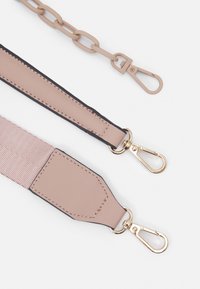 Två beige väskremmar med guld- och beige metallspännen på en vit bakgrund, en med kedjelänkar och en med tyg och läder.