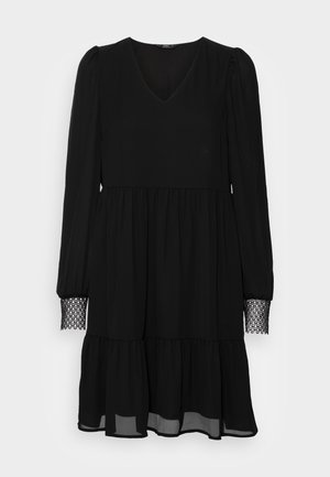 Black dress with long sleeves, V-neck, tiered skirt, and lace detail at the sleeve cuffs. Made from a flowing fabric, semi-sheer hem.