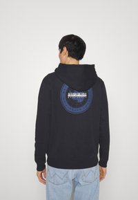 Sudadera negra con capucha que tiene un gráfico circular azul en la espalda, con texto y un diseño de un mapa mundial. Tela suave, ajuste cómodo.