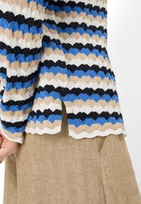 Strickpullover mit einem mehrfarbigen Zickzackmuster in Schwarz, Blau, Beige und Weiß; seitliche Schlitzdetails; weicher, strukturierter Stoff.