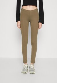 Olive green leggings with a smooth texture and elastic waistband, paired with gray sneakers featuring mesh and rubber accents.