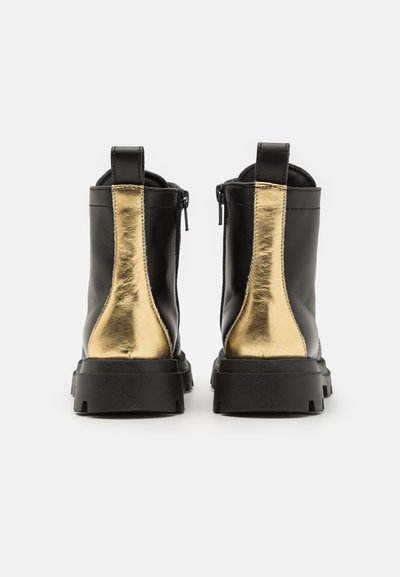 Botas de cuero negro hasta el tobillo con acentos metálicos dorados, vista trasera, con un acabado texturizado, suelas gruesas negras y cierre de cremallera.
