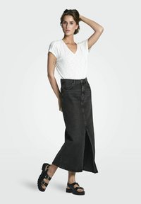Zwarte denim maxi-rok met een voorknoop, gecombineerd met een witte T-shirt met korte mouwen en een V-hals, en zwarte chunky sandalen met gespen.