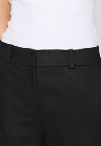 Pantalones negros con una textura suave, frente plano y una cinturilla estrecha. La tela parece ligera y ligeramente drapeada.
