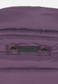 Fioletowa pikowana tkanina z małą czarną prostokątną metką z napisem „camel active” przyszytą między dwoma metalowymi oczkami.