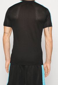 Schwarzes Sportshirt mit kurzen Ärmeln, mit türkisfarbenen Akzenten an den Schultern. Aus atmungsaktivem Mesh-Gewebe gefertigt.