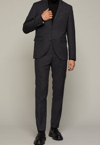 Grå rutmönstrad kostym med skräddarsydd passform, med kavaj med två knappar och smala byxor. Matchad med svarta oxfordskor.