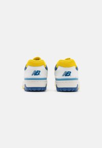 Par de zapatillas New Balance con acentos en blanco, azul y amarillo, mostradas desde la parte trasera sobre un fondo claro liso.