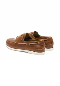 Bateaux en cuir marron avec un bout rond, semelle blanche contrastante, lacets en cuir et œillets en métal. Coutures détaillées autour des bords.