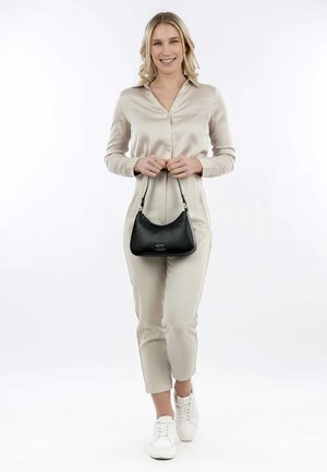 Zwarte nepleren handtas met een ronde vorm, voorzien van een korte schouderband en zilveren accenten. Het model draagt een satijnen beige blouse en lichte broek.