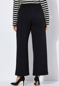 Zwarte wijde broek met een gladde textuur en een hoge tailleband. Gekoppeld met zwarte hoge hakken. De achtergrond is eenvoudig wit.