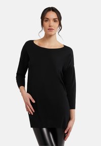 Svart långärmad tunika i mjukt tyg, med vid halsringning och avslappnad passform, med mjuk textur och minimala detaljer.