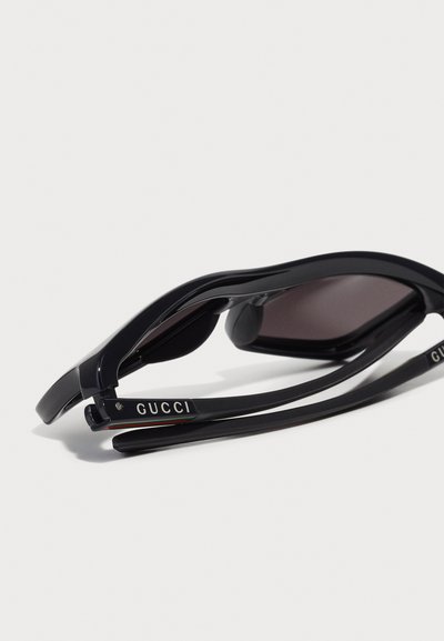 Mustad mustaklaasid sujuva disainiga, tumendatud läätsed ja silmapaistev "GUCCI" logo templil. Omab siledat pinda ja kumerat kuju.