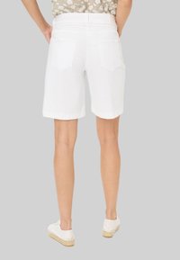 Witte denim shorts met een fitted taille, opgerolde zoom en twee achterzakken. Gecombineerd met witte espadrilles op een grijze achtergrond.