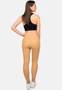 Leggings beige con una texture liscia e una vita alta, abbinati a un crop top sportivo nero e sneakers bianche. Vista da dietro.