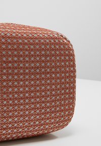Borsa strutturata in arancione ruggine con motivo a diamante, con dettagli argentati intrecciati, angoli arrotondati e una finitura liscia.