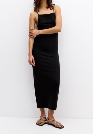 Sort figursyet maxikjole med tynde stropper, glat tekstur og en lige silhuet. Båret med neutrale flade sandaler. Enkel design.