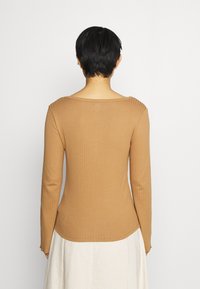 Haut à manches longues en tissu côtelé de couleur marron clair. Il présente un large décolleté et une forme ajustée, avec de l'élasticité pour le confort. Aucun motif visible.