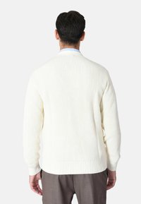 Cardigan in maglia a costine color crema con maniche lunghe, collo rotondo e polsini a costine. Texture visibile e design senza cuciture sulla schiena.