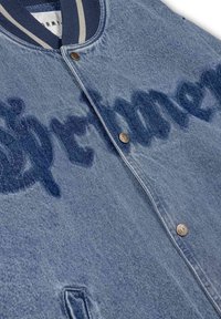 Chaqueta de mezclilla con un diseño clásico, color azul, cuello acanalado, botones de latón y un efecto de letras descoloridas a lo largo de la tela.