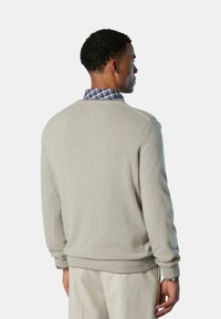 Maglione grigio chiaro in morbido tessuto a maglia, con scollo rotondo e polsini a coste. Indossato sopra una camicia a quadri blu e bianca.