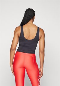 Sort tætsiddende tank top parret med højtsiddende, blanke røde leggings med hvid logo tekst, set bagfra.
