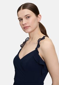 Granatowa sukienka z falbaniastymi, przezroczystymi ramiączkami, głębokim dekoltem w kształcie litery V oraz dopasowanym gorsetem. Gładka faktura o klasycznym designie, idealna na formalne okazje.