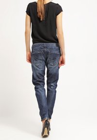 Vaqueros de mezclilla azul oscuro con un corte ajustado, que cuentan con cinco bolsillos y una textura descolorida, combinados con una camisa negra de manga corta y tacones.