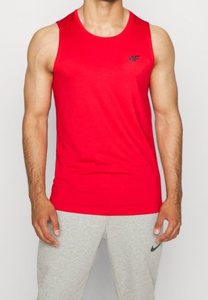 Mężczyzna w czerwonej sportowej koszulce bez rękawów z czarnym logo na klatce piersiowej oraz w jasnoszarych spodniach dresowych z czarnym logo Nike.