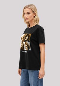 Black cotton t-shirt featuring a graphic print of four faces in sepia tones; text "LET IT BE" printed below the images. Short sleeves.