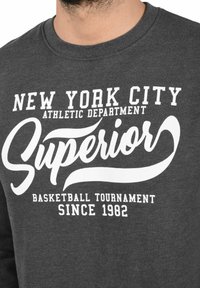 Dark gray sweatshirt featuring white graphic text: "NEW YORK CITY ATHLETIC DEPARTMENT," "SUPERIOR," and "BASKETBALL TOURNAMENT SINCE 1982."