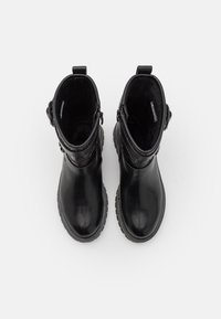 Bottes noires à cheville avec une tige en cuir lisse, bout rond et une bande texturée en haut, avec une semelle en caoutchouc et une fermeture éclair sur le côté.