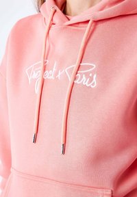 Sweat à capuche rose corail avec texte brodé blanc "Project x Paris", doté de cordons de serrage avec embouts argentés et d'une poche avant. Texture douce en mélange de coton.