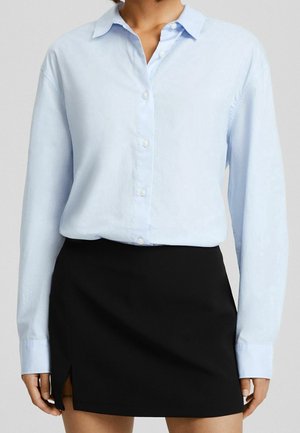 Camicia azzurra chiara a maniche lunghe con bottoni, colletto a punta e vestibilità comoda, abbinata a una mini gonna nera con una spacco laterale.