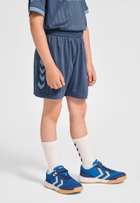 Blaue Sportshorts mit elastischem Bund und hellen Streifen. Kombiniert mit blauen Turnschuhen mit weißen Akzenten und weißen Socken.