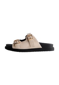 Sandalias de deslizamiento beige claro con dos correas ajustables, hebillas en tono dorado y una suela de goma negra, con una textura suave y un diseño minimalista.