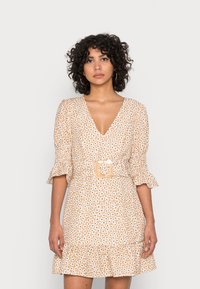 Vestido com padrão floral em bege e creme, apresentando um decote em V profundo, mangas bufantes, cintura ajustada com uma fivela quadrada e uma barra em camadas.