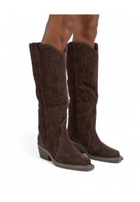 Botas de cuero ante marrón de vaquero con puntera puntiaguda, patrones de costura detallados y tacón apilado. Diseñadas para cubrir hasta la rodilla.