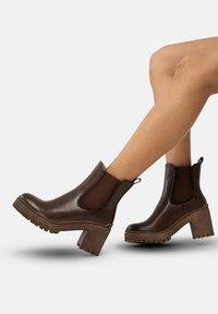 Bruna läderankelstövlar med elastiska sidopaneler, kraftig blockklack och texturerad sula. Har en dragflik för lätt av- och påtagning.