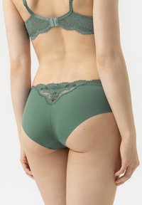 Groene kant en stof ondergoed met een hoog gesneden ontwerp, met ingewikkelde kant afwerking aan de achterkant en een gladde textuur overal.